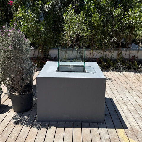 Modern outdoor fire pit on a wooden deck with greenery in the background