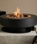 Modern fire pit with logs and a blanket on a concrete surface against a beige wall.