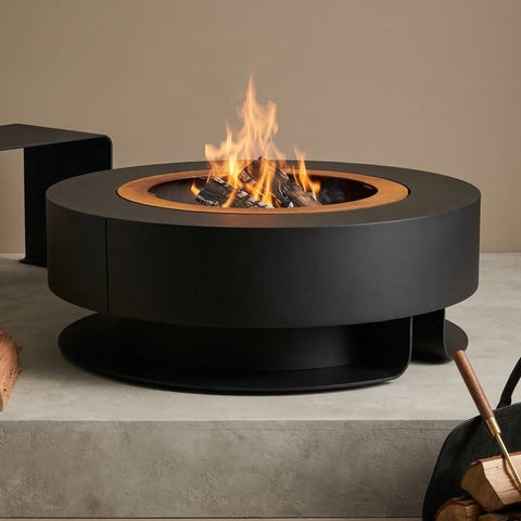 Modern fire pit with logs and a blanket on a concrete surface against a beige wall.