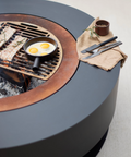 Round fire pit table with grill and cooking pan on a neutral background