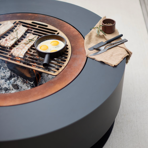 Round fire pit table with grill and cooking pan on a neutral background